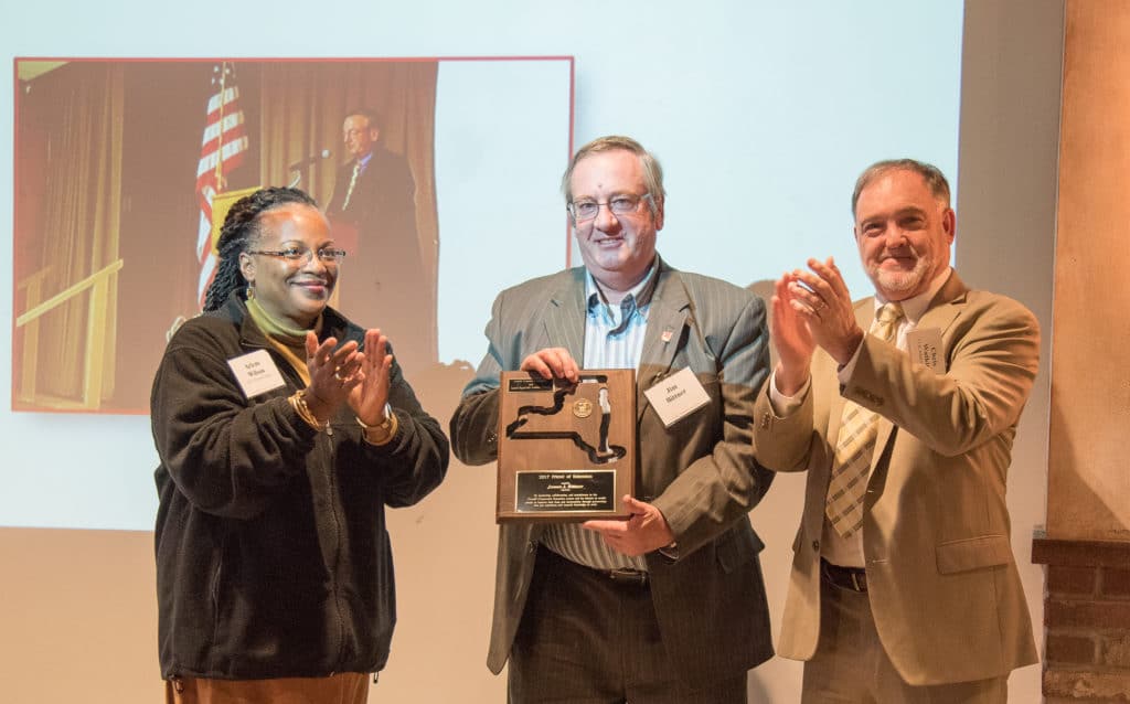 three people, one holding a plaque and the other two clapping