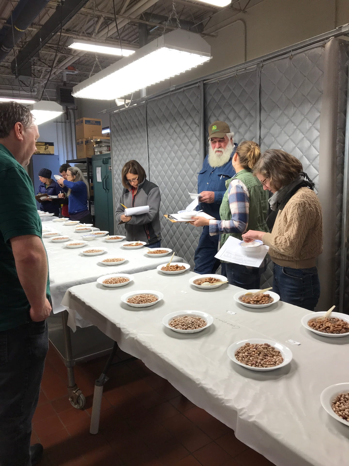 several people stand around a long table containing a selection of many dried beans