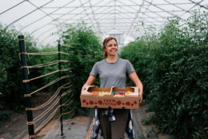 a person stands in a greenhouse holding a box of tomatoes