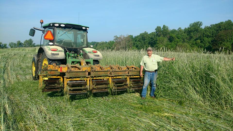 Steve Groff of Cedar Meadow Farm stands next to his tractor, which is pulling a roller-crimper he developed. 