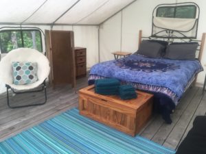 The inside of a glamping tent, fully furnished with a bed, a chair, and decor.