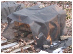 Logs stacked underneath a black agricultural tarp.