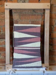 Purple, pink, and white fibers woven in a loom