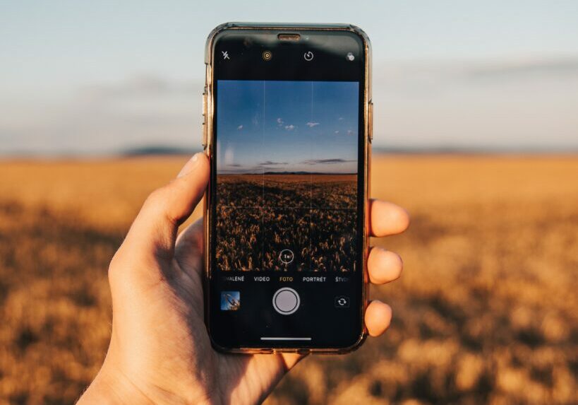 Image of hand holding smartphone with field and sky in distance.