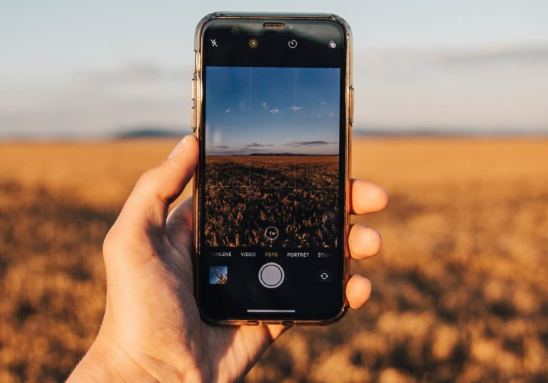 Image of hand holding iphone with field and sky in distance.