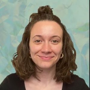 A woman with shoulder-length brown hair, styled with the top section pulled up, is smiling softly. She is wearing a black top and gold hoop earrings, with a pastel blue and green abstract background featuring small farms courses behind her.